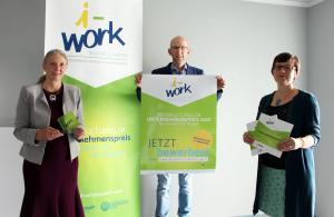 Zwei Frauen und ein Mann präsentieren den „i-work Business Award 2020“ sowie das i-work-Plakat und die aktuelle Broschüre.