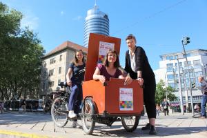 Drei Frauen sind an einem Lastenrad postiert und präsentieren das Plakat zum Tag der Vielfalt in Jena.