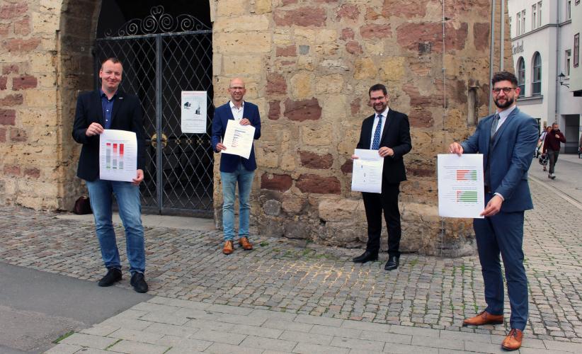 Vier Männer stehen vor dem historischen Rathaus in Jena und präsentieren die Ergebnisse der Unternehmensbefragung.