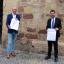 Zwei Männer stehen vor dem historischen Rathaus in Jena und präsentieren die Ergebnisse der Unternehmensbefragung.