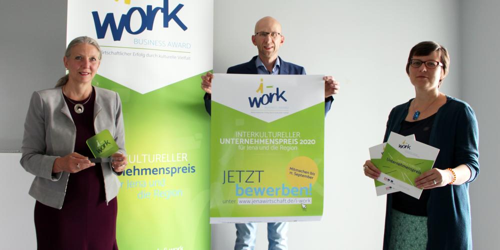 Zwei Frauen und ein Mann präsentieren den „i-work Business Award 2020“ sowie das i-work-Plakat und die aktuelle Broschüre.