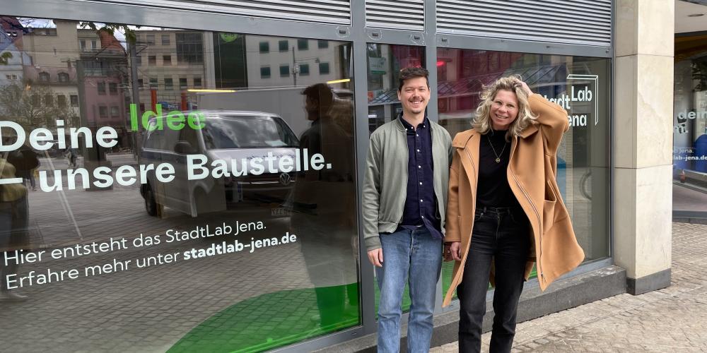 Ein Mann und eine Frau stehen vor der Schaufensterscheibe der neuen Räumlichkeiten des StadtLab Jenas.