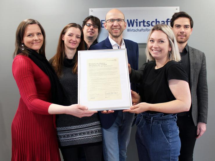 Gruppe von 6 Personen halten Bilderrahmen mit Urkunde