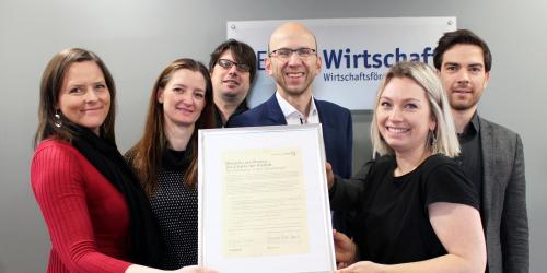 Gruppe von 6 Personen halten Bilderrahmen mit Urkunde