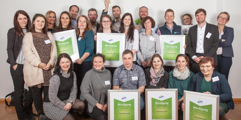 Gruppe von etwa 30 Personen sitzend und stehend, halten Bilderrahmen mit Urkunden in der Hand