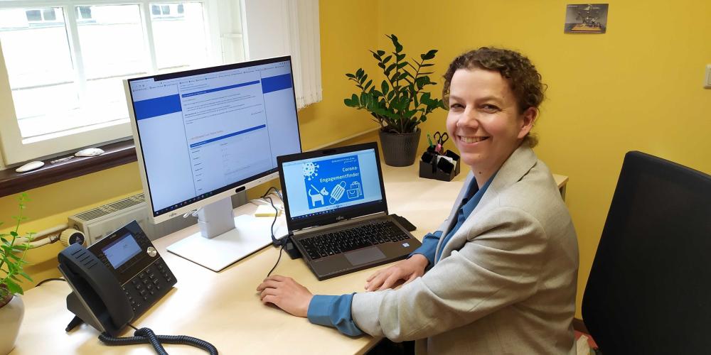 Frau sitzt am Schreibtisch vor Computer auf dem Webseite des Engagementfinders geöffnet ist