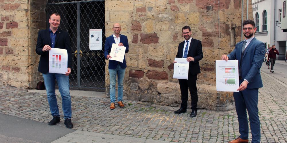 Vier Männer stehen vor dem historischen Rathaus in Jena und präsentieren die Ergebnisse der Unternehmensbefragung.