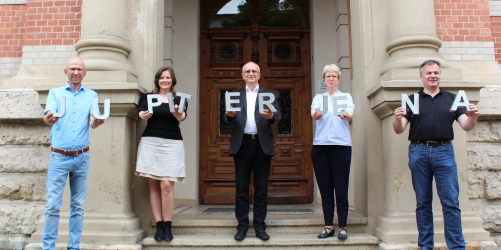 Fünf Personen stehen auf Treppe und halten Buchstaben hoch