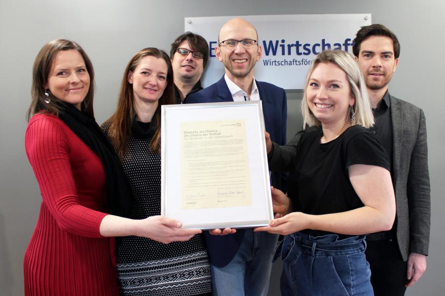 Gruppe von 6 Personen halten Bilderrahmen mit Urkunde