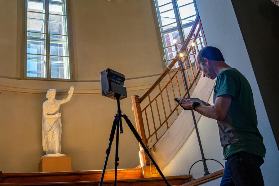 Mann erstellt mit einer Kamera eine 3D-Aufnahme in einem Raum mit einer Holztreppe und großen Fenstern. Stadtmuseum.