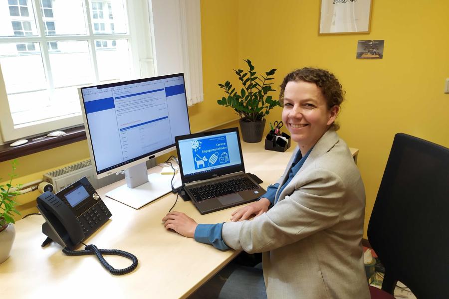 Frau sitzt am Schreibtisch vor Computer auf dem Webseite des Engagementfinders geöffnet ist