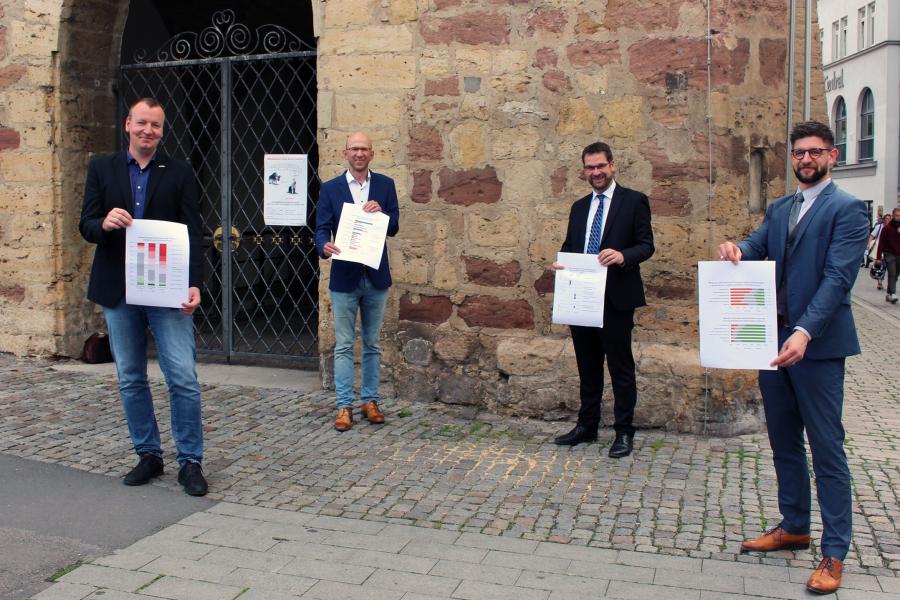 Vier Männer stehen vor dem historischen Rathaus in Jena und präsentieren die Ergebnisse der Unternehmensbefragung.