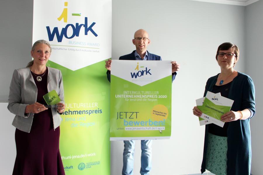 Zwei Frauen und ein Mann präsentieren den „i-work Business Award 2020“ sowie das i-work-Plakat und die aktuelle Broschüre.