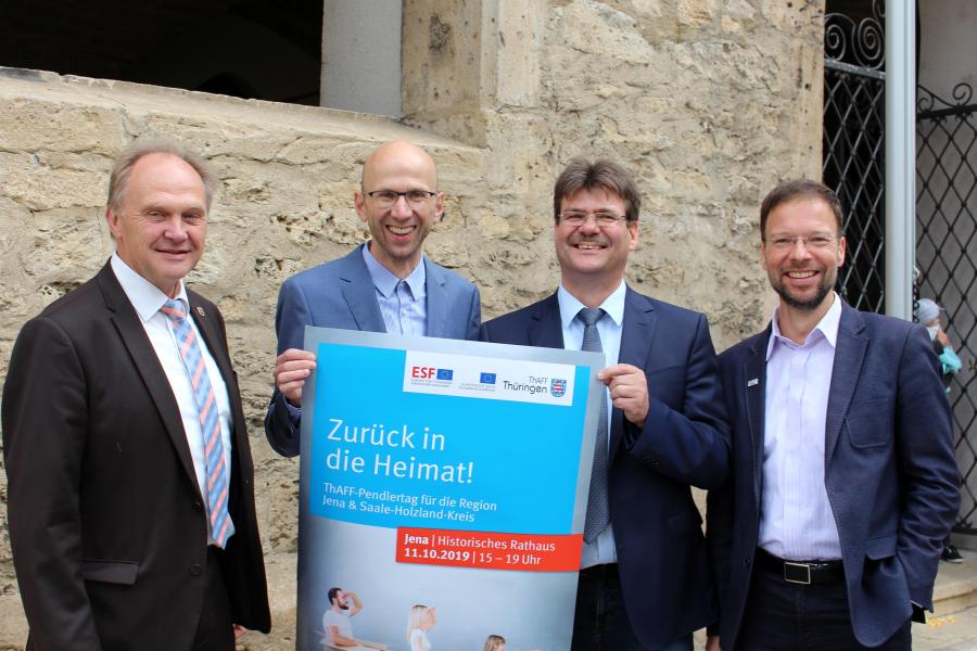 Vier Männer stehen nebeneinander und halten das Plakat für den Pendlertag in die Kamera.