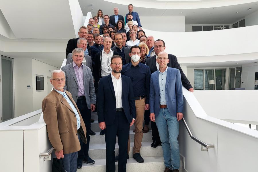 Rund 40 Jenaer Unternehmer:innen posieren auf dem Wirtschaftsaustausch in Erlangen auf einer Treppe.