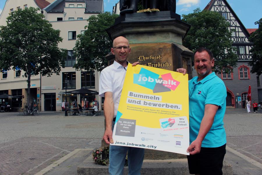 Zwei Männer präsentieren das Plakat vom jobwalk Jena, einer Open-Air-Jobmesser auf dem Jenaer Marktplatz.