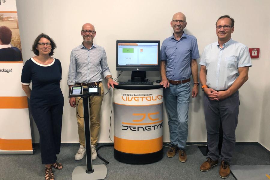 Eine Frau und drei Männer stehen neben einerm Fingerabdruckscanner der Firma Jenetric und schauen in die Kamera.