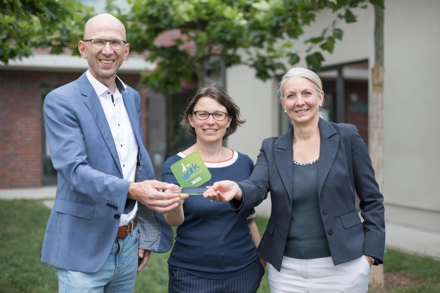 Drei Personen präsentieren einen Preis. 