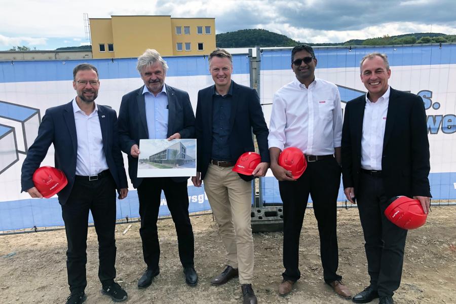 Fünf Personen mit Bauhelmen posieren vor der zukünftigen Baustelle.