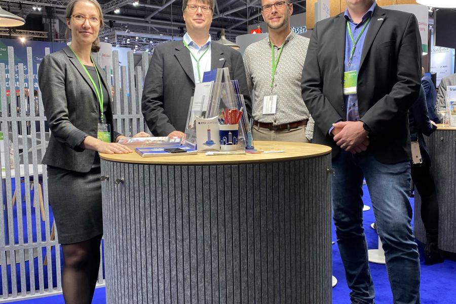 Vier Personen posieren an einem Messestand